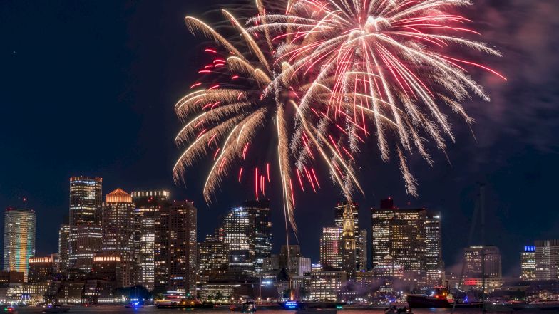 Fireworks over a city skyline at night reflected on the water, celebrating a festive occasion.