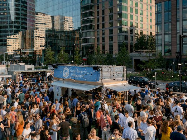 Outdoor event with a crowd, food truck, and modern buildings.