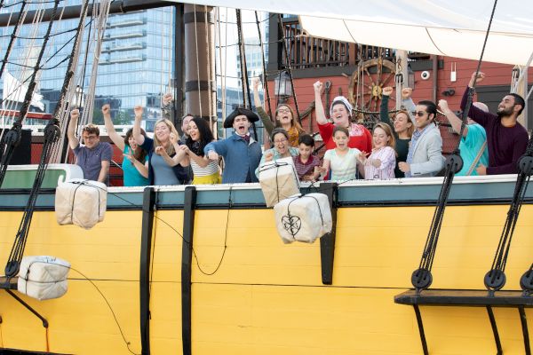 Guests on a yellow ship reenacting the throwing of the tea into Boston Harbor.
