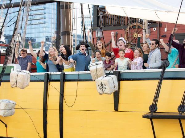 Guests on a yellow ship reenacting the throwing of the tea into Boston Harbor.