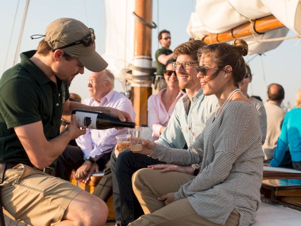 A group of people is enjoying a boat ride while a server pours a drink for a woman in a striped shirt.
