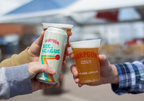 Three hands are holding beer: one holding a can and two holding plastic cups, all branded "Harpoon".