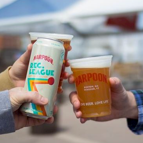 Three hands are holding beer: one holding a can and two holding plastic cups, all branded "Harpoon".