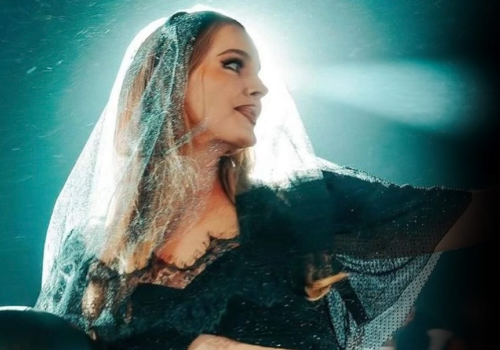 A person wearing a dark outfit and a veil, illuminated from behind, is looking to the side against a teal background ending the sentence.