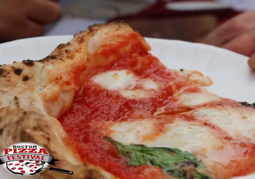 Close-up of a slice of Margherita pizza on a white plate, with a "Boston Pizza Festival" logo in the corner.