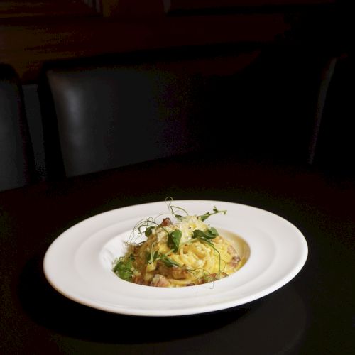 A plated dish of creamy risotto or pasta with herbs on a white plate, set on a dark table in low lighting.