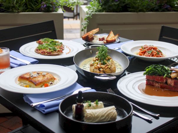 A variety of plated dishes on a table including salads, meat, pasta, a soup or sauce bowl, and drinks, all arranged beautifully for a meal.