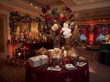 A festive holiday banquet setting with candles, a flower centerpiece, and twinkling Christmas d&eacute;cor in a decorated hall.