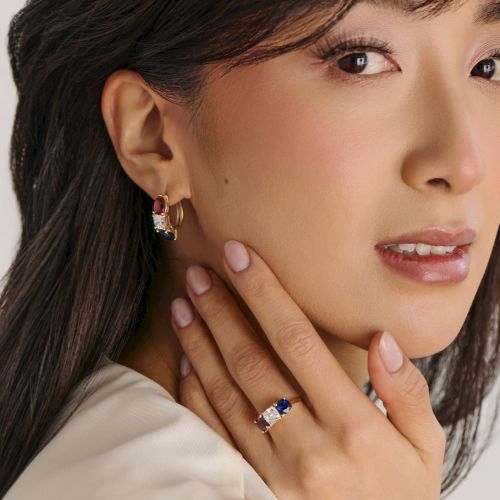 A close-up of a woman wearing elegant jewelry: dangling earrings with gems and a matching ring, showcasing a polished, sophisticated look.