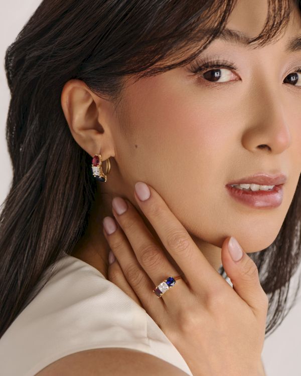A close-up of a woman wearing elegant jewelry: dangling earrings with gems and a matching ring, showcasing a polished, sophisticated look.