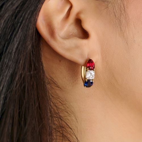 A small hoop earring with three colored stones (red, white, blue) set in a gold band, worn on the ear.