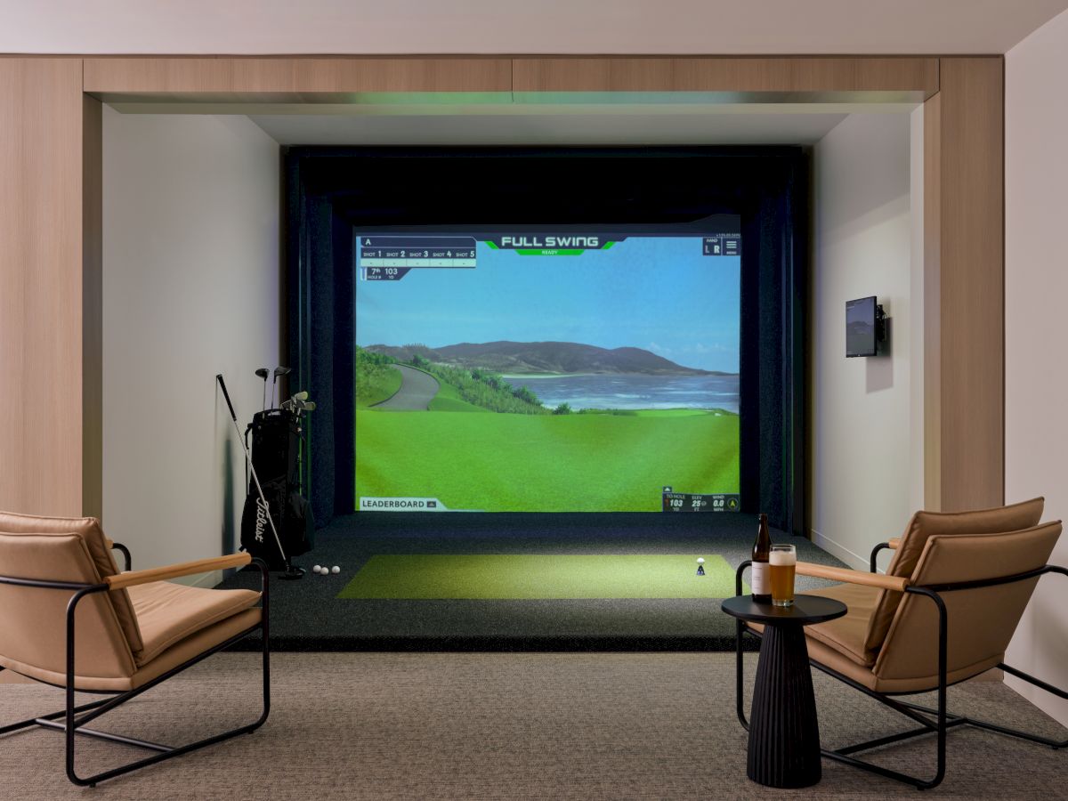 A home theater setup with a large screen showing a golf video, flanked by two tan chairs and a small table, creating a cozy viewing nook.
