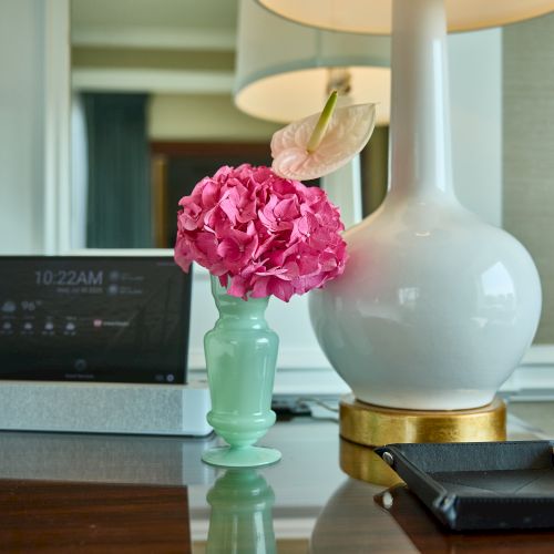 A desk scene with a laptop, a green vase holding pink flowers, a white decorative globe lamp, and a black pen case.