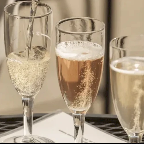 Three champagne flutes filled with sparkling beverages are placed on a table, with one being poured.