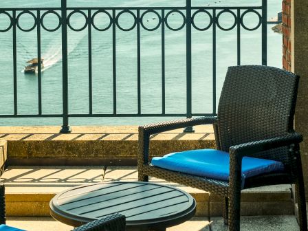 Wicker patio chair and table sit on a seaside terrace, with ocean waves visible through a decorative railing.