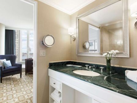Elegant bathroom with a marble countertop, large mirror, and adjacent sitting area.