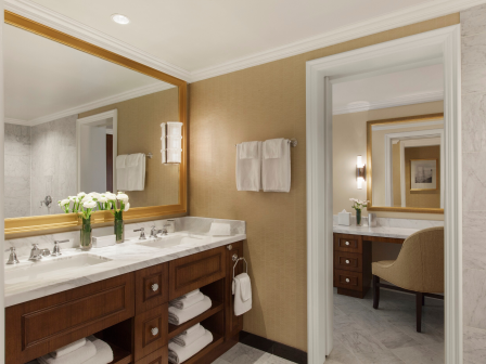 Elegant bathroom with dual sinks, mirrors, fresh flowers, and seating area.
