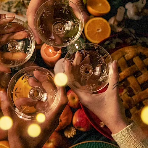 Friends clink patterned wine glasses filled with a sparkling drink around an outdoor autumn snack table. Cheers!