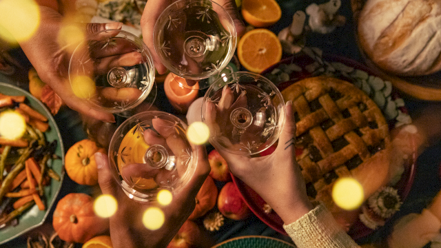 Friends clink patterned wine glasses filled with a sparkling drink around an outdoor autumn snack table. Cheers!
