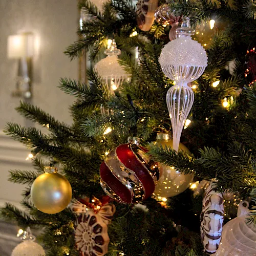 A decorated Christmas tree with warm gold lights and glass ornaments, including icicles, baubles, and snowflake-style decorations.