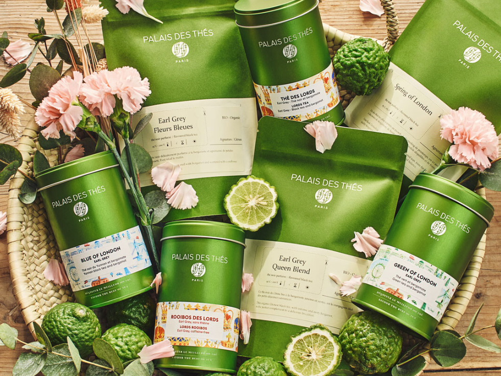 Assorted Palais des Th&eacute;s tea gift set in green tins and bags, with limes, flowers, and leaves on a wooden table.