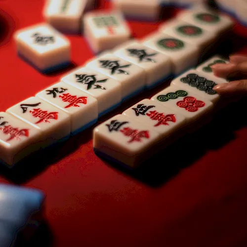 Mahjong tiles with colorful symbols are stacked on a red table, ready for a game.