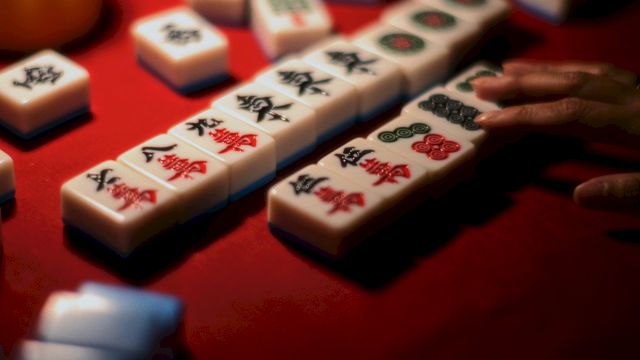 Mahjong tiles with colorful symbols are stacked on a red table, ready for a game.