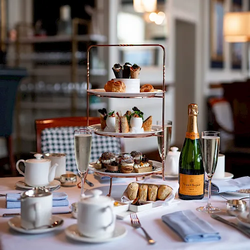 A festive afternoon tea setup with a three-tier tray of pastries and sandwiches, champagne bottle and glasses on a table.