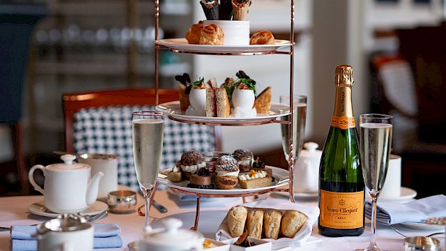 A festive afternoon tea setup with a three-tier tray of pastries and sandwiches, champagne bottle and glasses on a table.