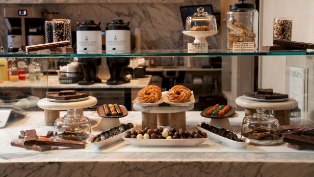 A dessert buffet display with chocolate treats, pastries, biscotti, and candy balls behind a glass case, ready to grab.