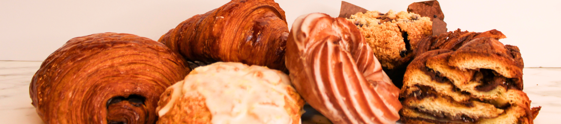An assortment of pastries, including croissants, a glazed bun, a muffin, and a swirled pastry, arranged on a marble surface.