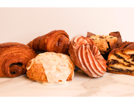 An assortment of pastries, including croissants, a glazed bun, a muffin, and a swirled pastry, arranged on a marble surface.