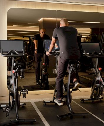 A person is exercising on a stationary bike in a gym room with multiple bikes and mirrored walls.