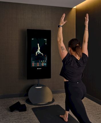 A person is doing yoga in front of an interactive workout screen, following an on-screen instructor in a modern room.