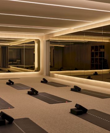 A yoga studio with mats, blocks, and ambient lighting, featuring large mirrors and shelves stocked with yoga props.