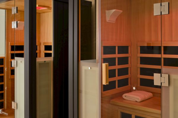 Two modern wooden infrared saunas with glass doors, featuring interior lights and a towel on one of the benches.
