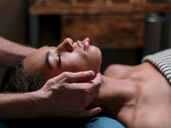 A person is receiving a relaxing massage in a dimly lit room with lit candles in the background, creating a serene atmosphere.