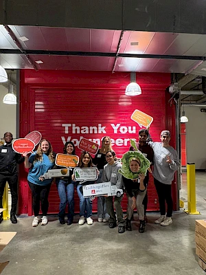 A group of people stand in a warehouse, holding signs in front of a red door that reads 