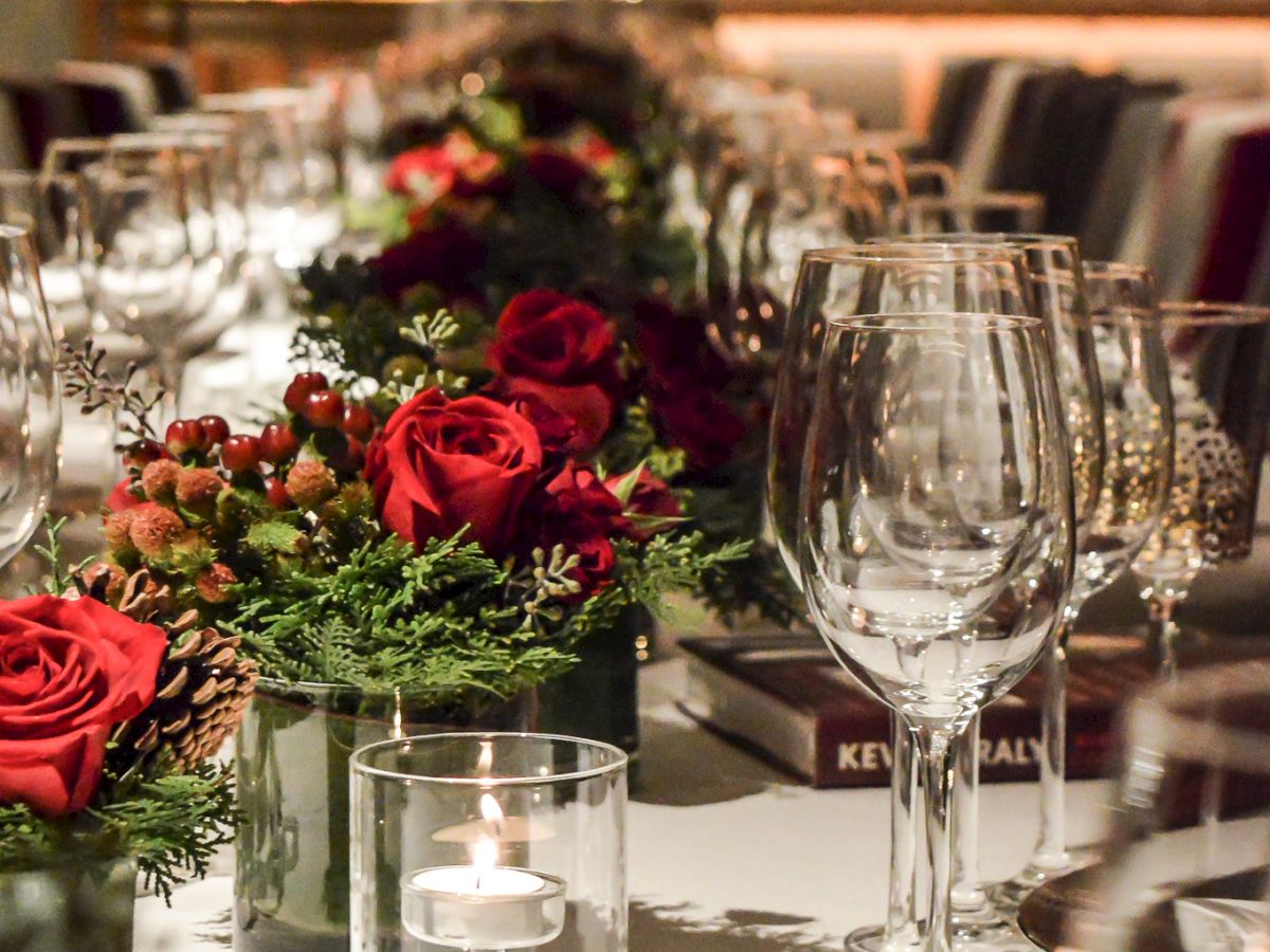 A beautifully set dining table with red roses, greenery, wine glasses, and candles, creating an elegant and inviting atmosphere.